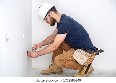 Electrician Builder at work, installation of sockets and switches. Professional in overalls with an electrician's tool. Against the background of the repair site. 