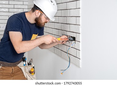 Electrician Builder at work, installation of sockets and switches. Professional in overalls with an electrician's tool. Against the background of the repair site. 