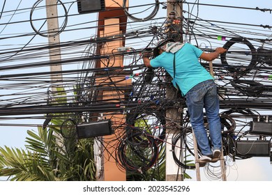 An electrician is climbing an electric pole to inspect and install wires without wearing protective equipment for safety from work risks.