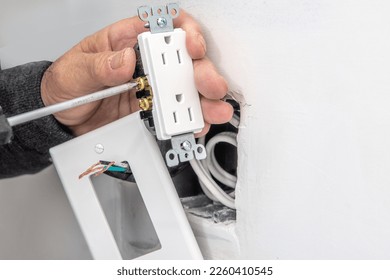 An electrician connects electrical wires to an outlet before installing it.