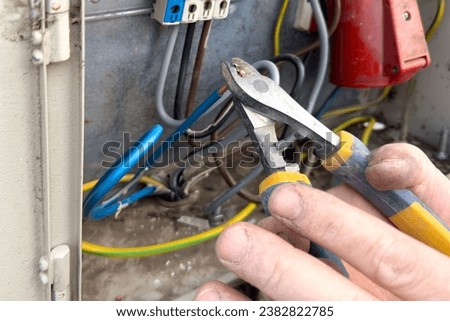 The electrician connects the wires in the shield. Hands of an electrician close-up with tongs cut off the ends of the wire before connecting in the electrical panel