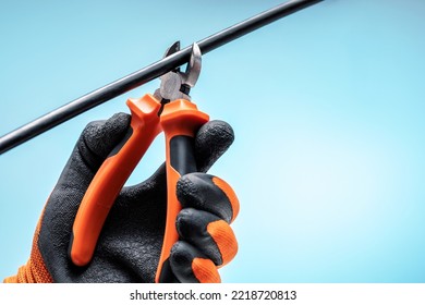 Electrician Cutting Wire With Pliers Against Blue Sky Background. Sabotage Concept.