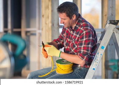 Electrician Cutting Wire Whilst Wiring Room On Indoor Building Construction Site