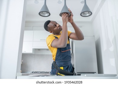 Elektriker. Dunkelhäutige Servicemann in gelbem T-Shirt zur Reparatur von Stromlampen