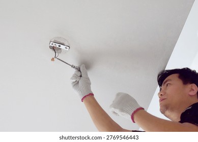 The electrician is disassembling the ceiling light fixture.
