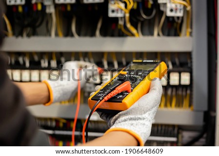 Electrician engineer uses a multimeter to test the electrical installation and power line current in an electrical system control cabinet.