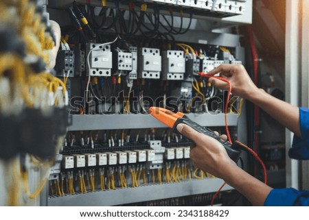 Electrician engineer uses a multimeter to test the electrical installation and power line current in an electrical system control cabinet.
