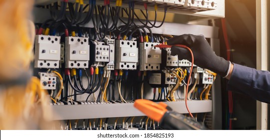 Electrician engineer work tester measuring voltage and current of power electric line in electical cabinet control.and wires on relay protection system. Bay control unit. Medium voltage switchgear. - Shutterstock ID 1854825193