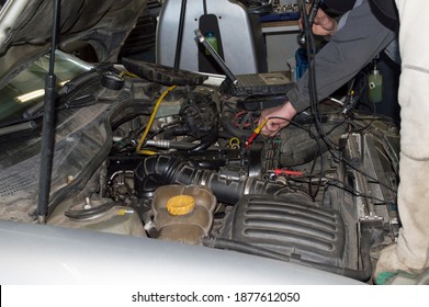 An Electrician In A Gray Uniform Checks The Electrical Equipment Under The Hood Of The Car Using A Computer In The Car Repair Shop