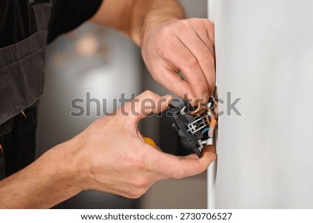 Electrician hands installing electrical light switch with exposed wires into wall socket during home renovation. Concept of electrical work, maintenance, repair and household improvement