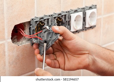 Electrician Hands Tighten Electrical Wires In Wall Fixture Or Socket Using A Screw Driver - Closeup