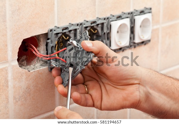 Electrician hands tighten\
electrical wires in wall fixture or socket using a screw driver -\
closeup