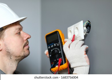 Electrician In Helmet Measures Level Electricity. Combined Electrical Measuring Instrument, Combining Several Functions. Handheld Multimeter For Basic Measurements And Troubleshooting At Outlet