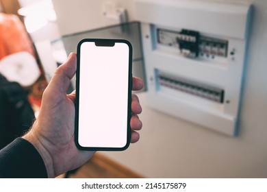 Electrician Holding Smartphone With Blank Mockup Touch Screen In Front Of Circuit Breaker Box At Home, Selective Focus