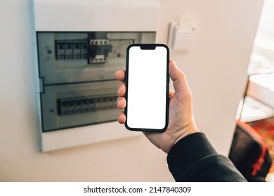 Electrician Holding Smartphone With Blank Mockup Touch Screen In Front Of Circuit Breaker Box At Home, Selective Focus