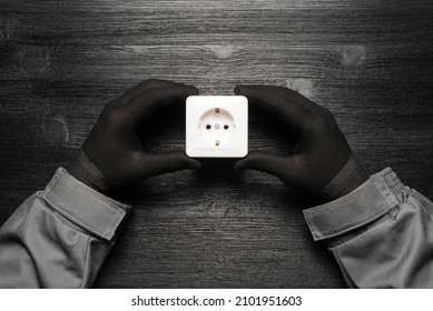 Electrician holds in the hands an electric power socket on the black flat lay wooden workbench background.