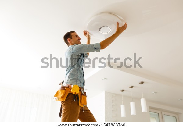 Electrician is installing and connecting a lamp\
to a ceiling.