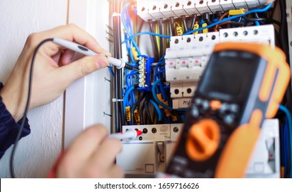 Electrician installing electric cable wires and fuse switch box. Multimeter in hands of electricians detail.