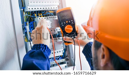 Electrician installing electric cable wires and fuse switch box. Multimeter in hands of electricians detail.