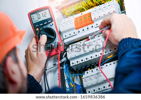 Electrician installing electric cable wires and fuse switch box. Multimeter in hands of electricians.