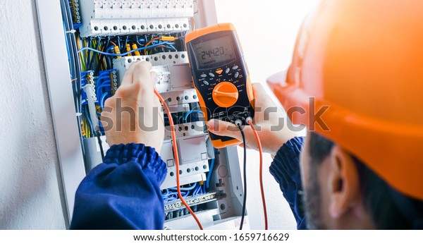 Electrician installing
electric cable wires and fuse switch box. Multimeter in hands of
electricians
detail.
