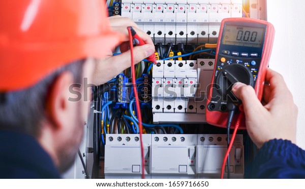 Electrician installing\
electric cable wires and fuse switch box. Multimeter in hands of\
electricians\
detail.