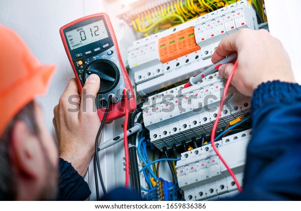 Electrician installing electric
cable wires and fuse switch box. Multimeter in hands of
electricians.