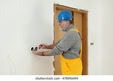 Electrician installing electrical plug at wall and using voltage testing screwdriver