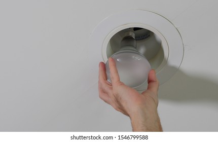 Electrician Installing New Light Bulb In Recessed Ceiling Light Fixture. Man Replacing Burned Out Incandescent Light Bulb.