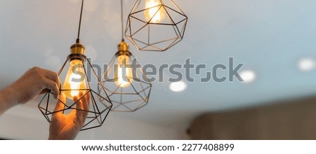 An electrician is installing spotlights on the ceiling. Handyman choosing between energy save and cheap incandescent lamp while changing light in the appartment