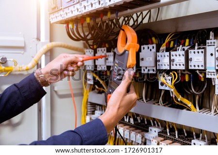 Electrician measurements with multimeter testing current electric in control panel.