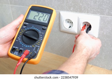 The electrician measures the voltage in the home network by inserting a voltmeter into the outlet. Measurement of voltage in electric networks - Shutterstock ID 2238547939