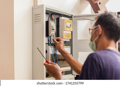 Electrician With Medical Mask Engineer Works With Electric Cable Wires Of Fuse Switch Box.