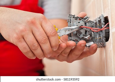 Electrician mounting the wires into electrical wall fixture or socket - closeup on hands and pliers