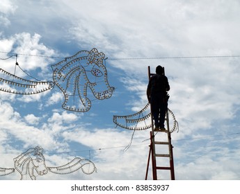 Electrician On A High Ladder Connecting Fair Illuminations , Doing A Dangerous Job At High Altitude