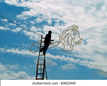 Electrician On A High Ladder Connecting Fair Illuminations , Doing A Dangerous Job At High Altitude