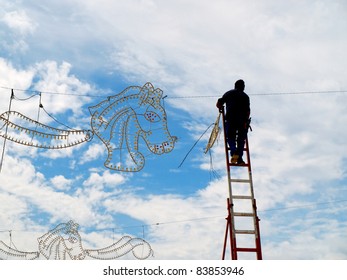 Electrician On A High Ladder Connecting Fair Illuminations , Doing A Dangerous Job At High Altitude