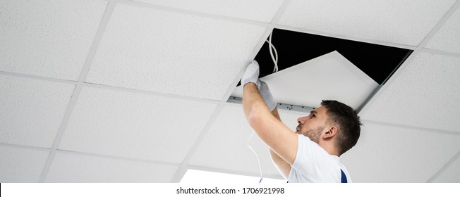 Electrician On Ladder Installing Office Lights On Ceiling