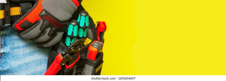 Electrician or professional Builder in the installer's belt with tools on a yellow background. Electrician's tools in black bags on the worker 's belt. Banner with space for text - Powered by Shutterstock