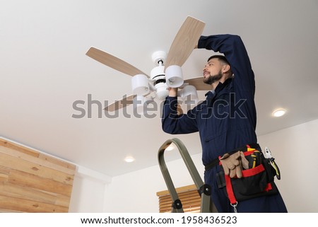 Electrician repairing ceiling fan with lamps indoors. Space for text