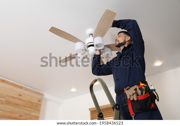 Electrician repairing ceiling fan with lamps\
indoors. Space for\
text