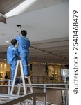 Electrician replacing ceiling light bulbs in the mall ,Thailand