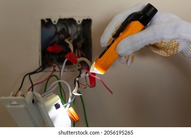 An electrician is replacing a wall switch. A DIY project concept. High voltage danger. A touchless voltage tester and protective rubber gloves are used. The tester has torch light for illumination