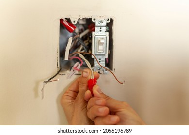 An electrician is replacing a wall switch. A DIY project concept. High voltage danger. She is working with bare hand tightening wires using plastic wirenut. There are labels on each wire 