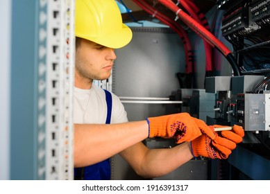 Electrician With Screwdriver And Pliers Tighten Up Switching Electric Actuator Equipment In Fuse Box.