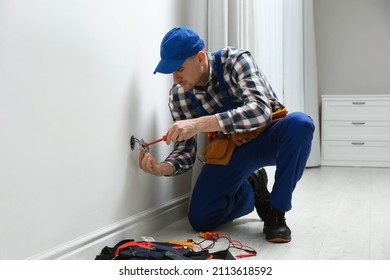 Electrician with screwdriver repairing power socket in room