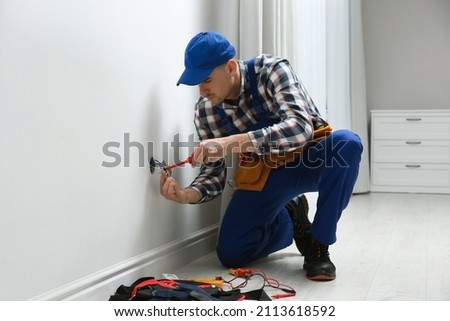 Electrician with screwdriver repairing power socket in room