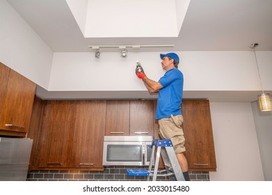 Electrician Standing On A Ladder Changing Out A Light Fixture On Track Lighting