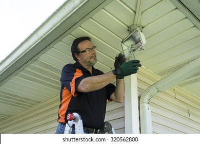 Electrician Taking Glass Cover Off Outside Light Fixture To Change Light Bulb.