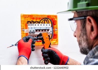 Electrician Technician With Helmet, Goggles And Gloves Protected Hands, Works With Wire Stripper In A Residential Electrical Panel.